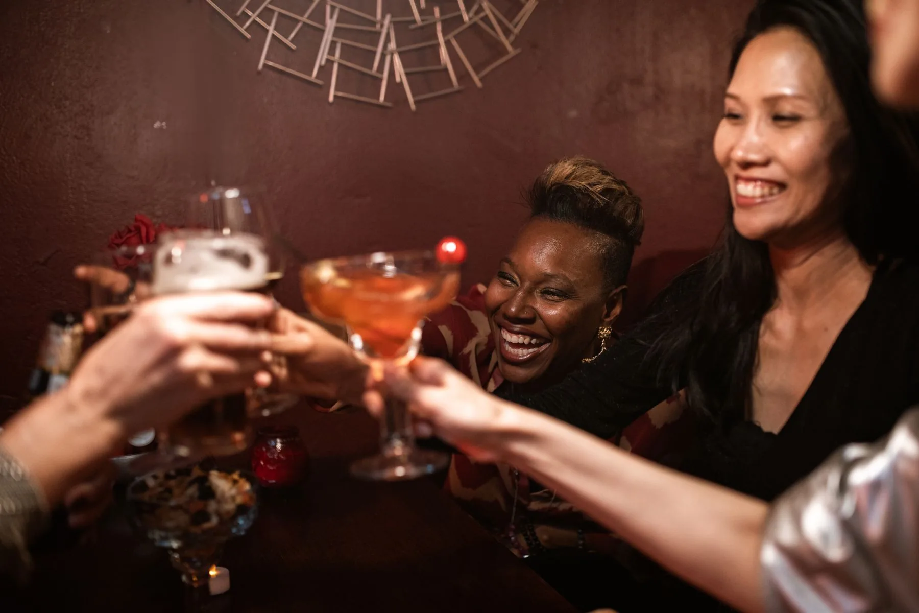 Friends laughing and raising cocktails together at the bar